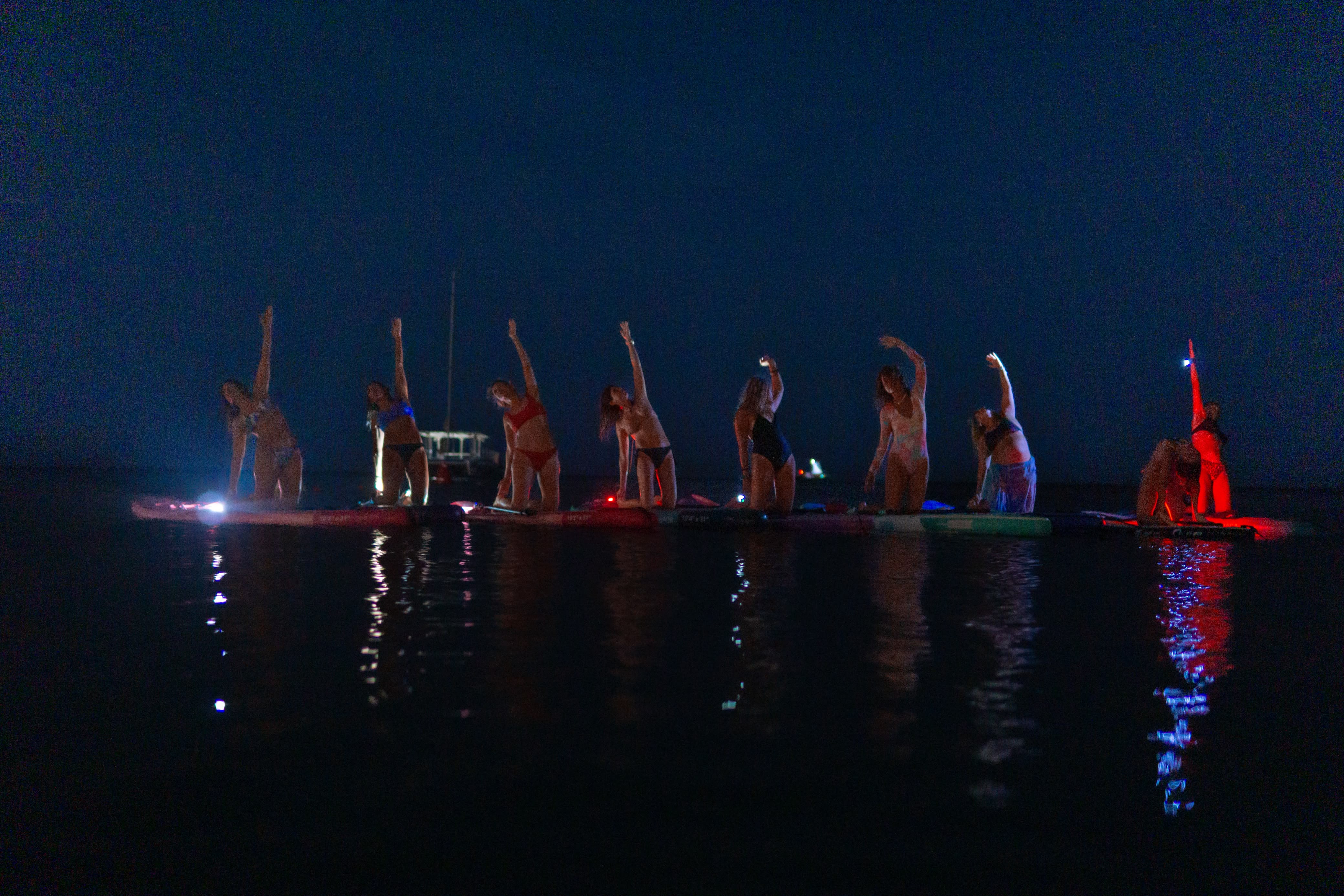 Night SUP yoga with lights reflecting on the water